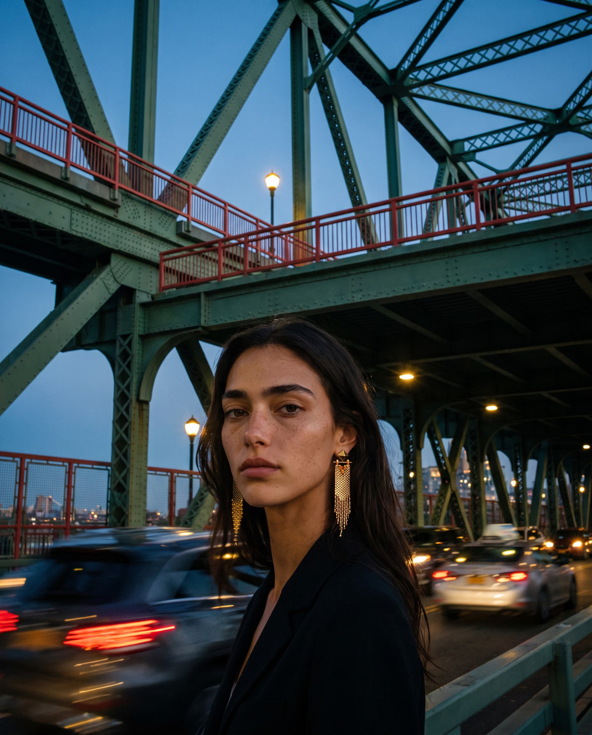 Woman wearing Amante gold fringe earrings on a New York bridge at dusk