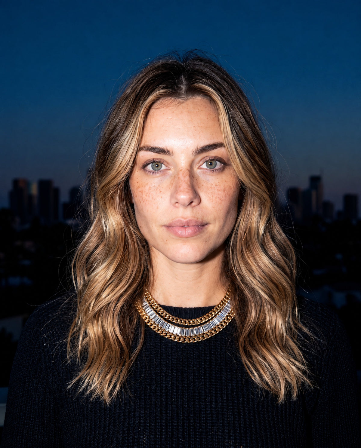 Woman wearing layered Amante gold chains with the New York skyline at dusk